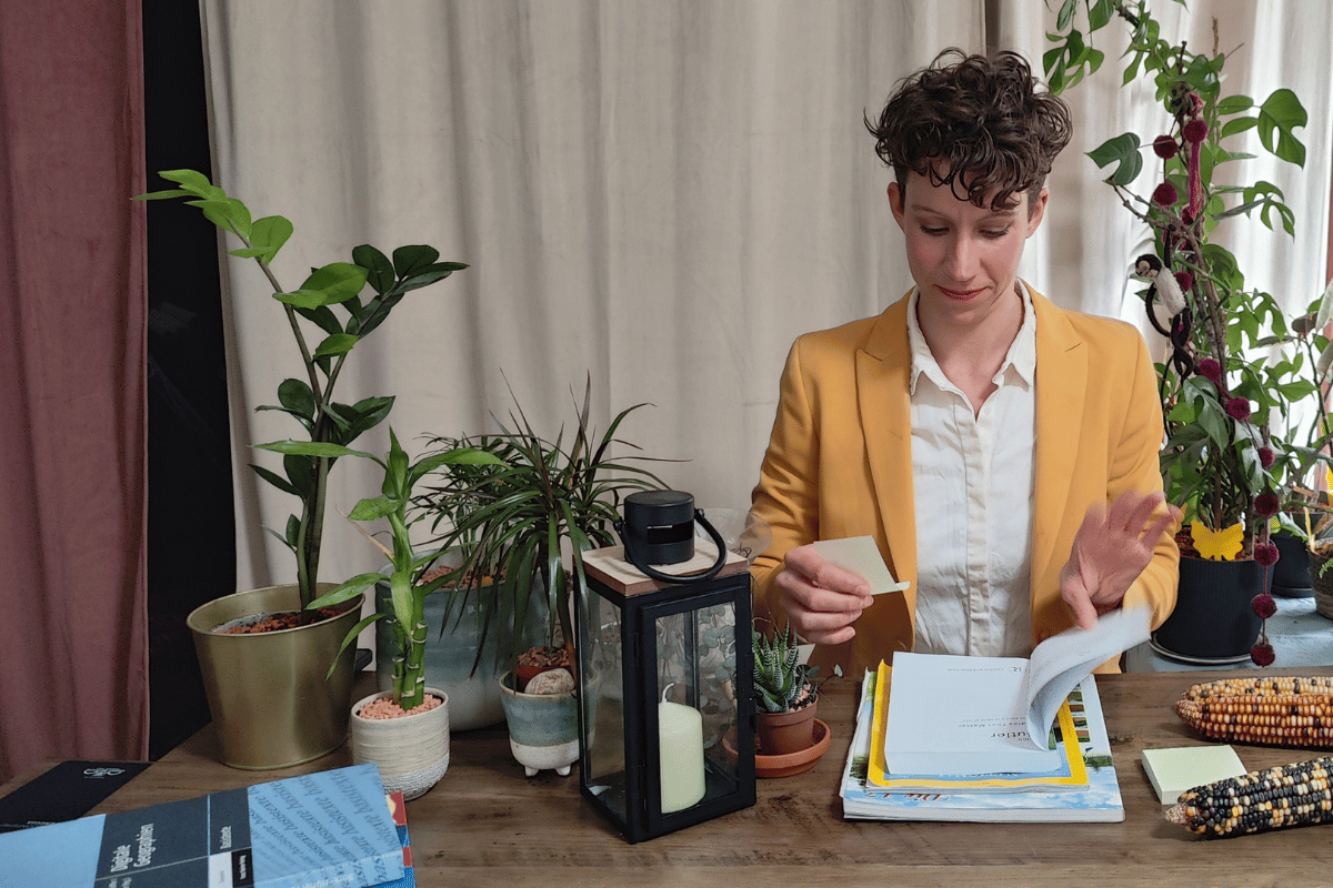 Scientist putting sticky notes in the book that lies on top of a pile of books on a table. On the side, there is a candle inside a glass candle holder.